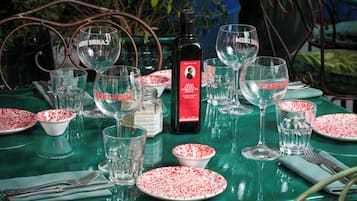 A table set with wine glasses, plates, and a bottle of wine, surrounded by chairs and greenery.