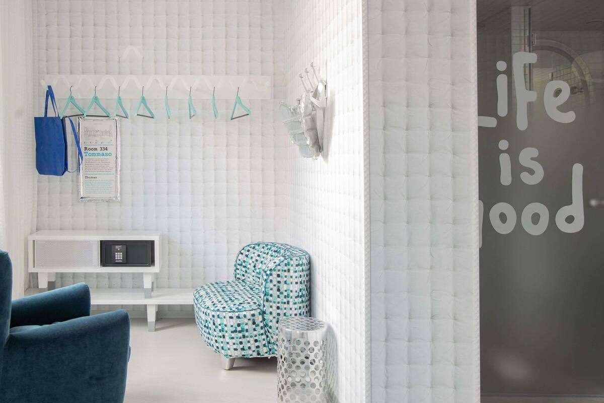 Une pièce moderne avec un mur blanc à texture, une chaise bleue, un pouf à motifs, un banc blanc et un panneau affichant un message.