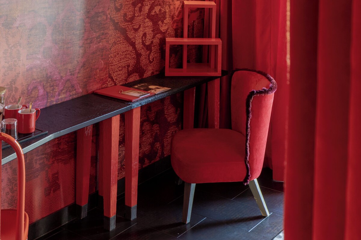 A room with a patterned wall, a red chair, a small table, and a wall-mounted light fixture.