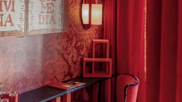 Una stanza con un muro decorato, una sedia rossa, un tavolino e un punto luce a parete.