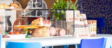 A breakfast buffet with various food items, including pastries, meats, and cheeses, displayed on a glass counter.