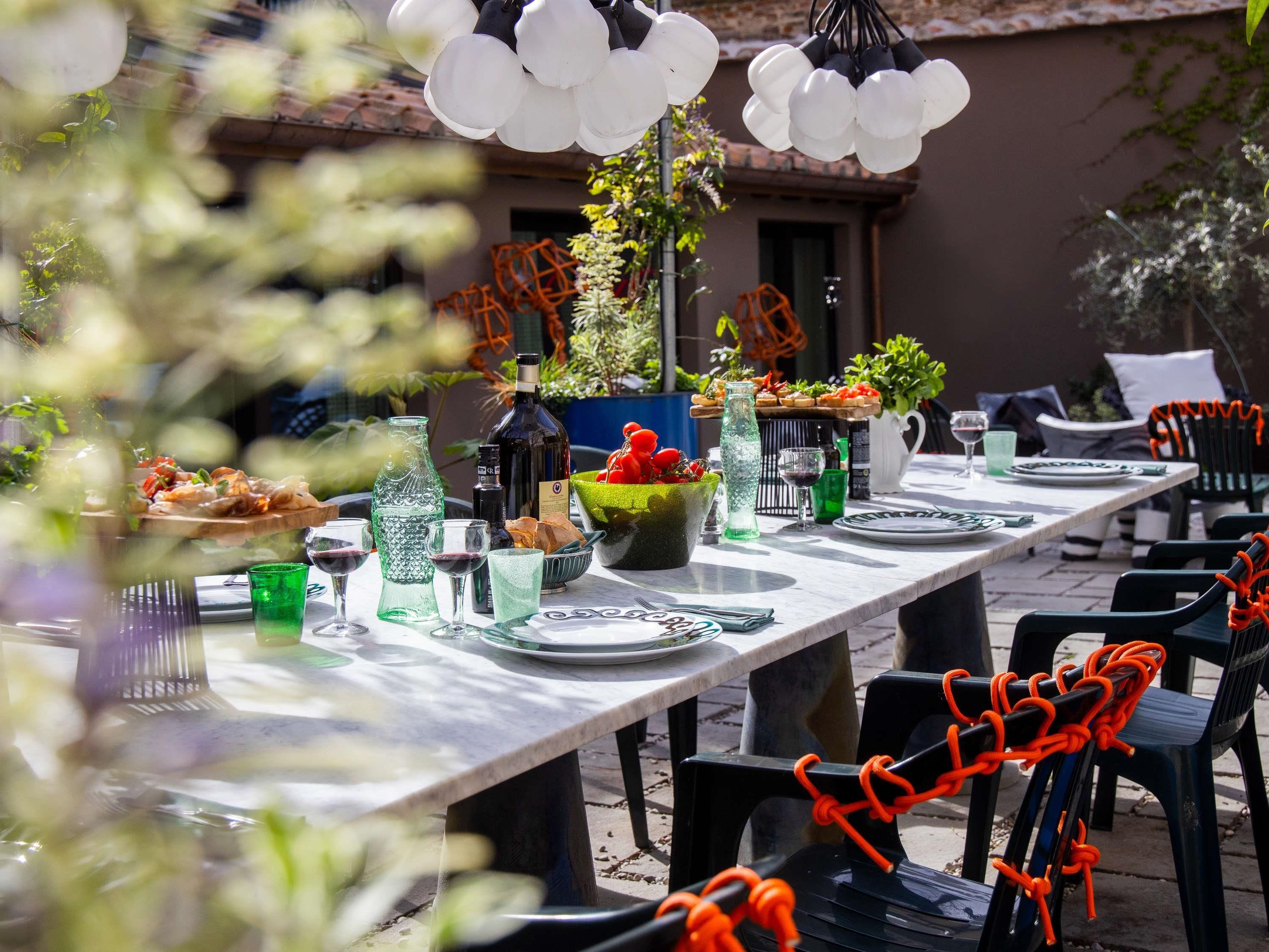 Een eettafel buiten met stoelen, een fles, glazen en een schaal fruit.