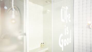 A modern bathroom with a glass shower enclosure, a white tiled wall, and a shelf with toiletries.