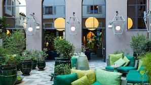 Un espace extérieur aménagé avec des meubles verts et des plantes en pot, un sol à carreaux et des fenêtres en arc de cercle.