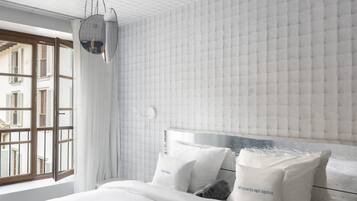 Quarto moderno com uma cama grande, roupa de cama branca e vista para edifícios através de janelas abertas.