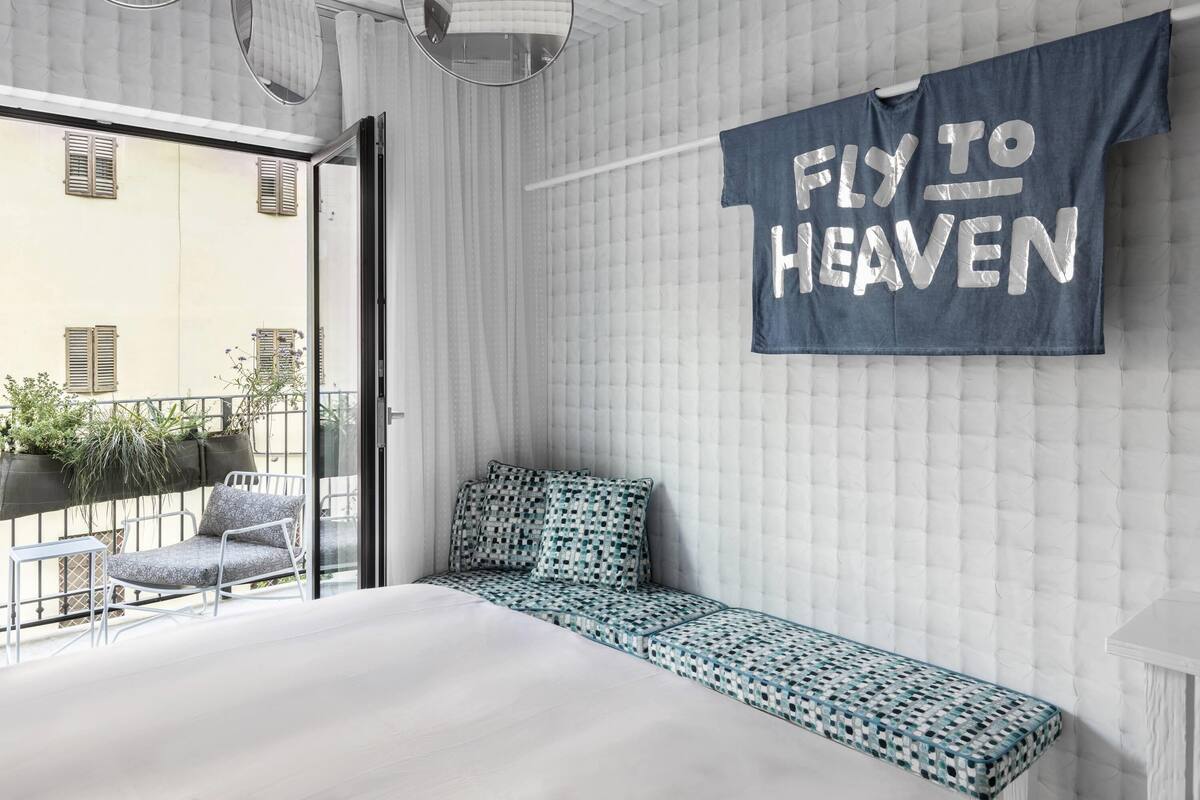 Une chambre à coucher moderne avec un lit, un banc, un panneau décoratif fixé au mur et un balcon agrémenté de plantes.