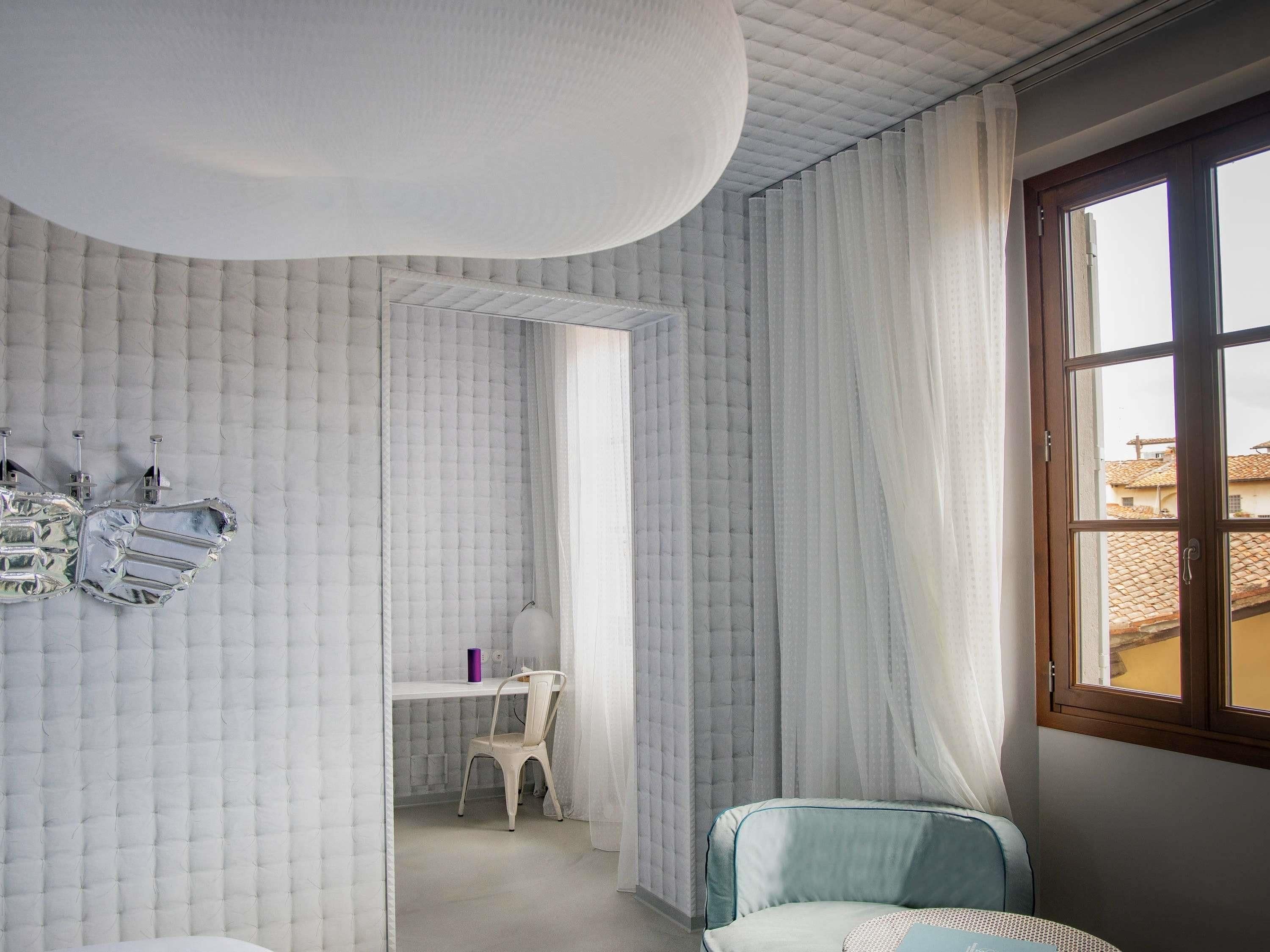 A room with a bed, a desk, and a chair. There is a window with curtains.