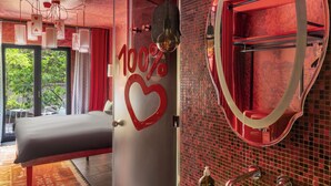 A modern hotel room with a large bed, a bathroom with a mosaic sink, and a glass door leading to a balcony.
