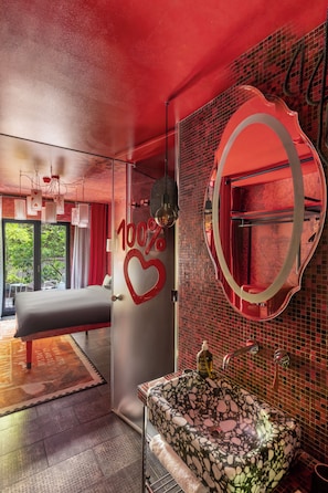 A modern hotel room with a large bed, a bathroom with a mosaic sink, and a glass door leading to a balcony. - 25hours Hotel Florence Piazza San Paolino (Florence)