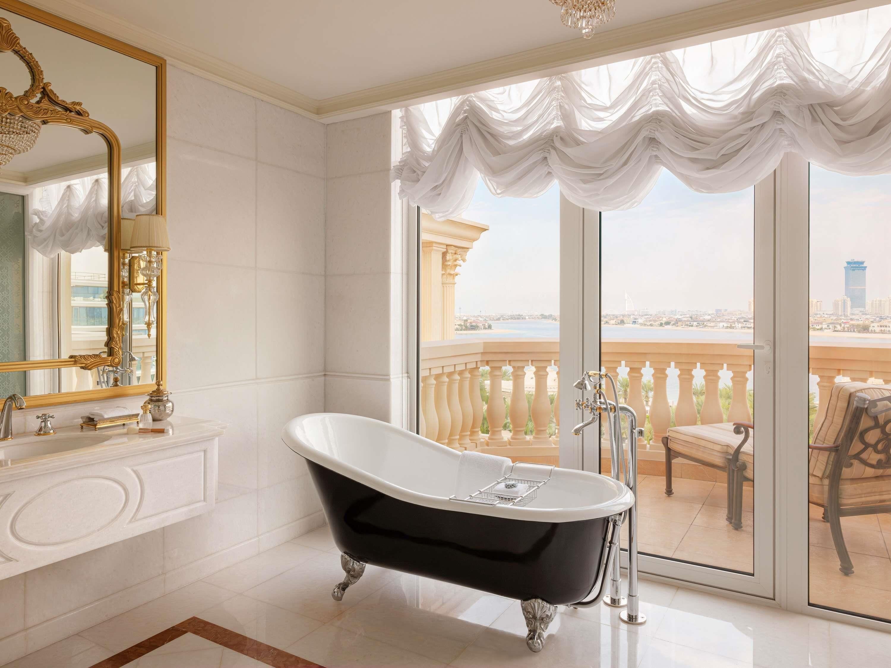 A bathroom with a freestanding bathtub, a large mirror, and a view of a cityscape through a balcony.
