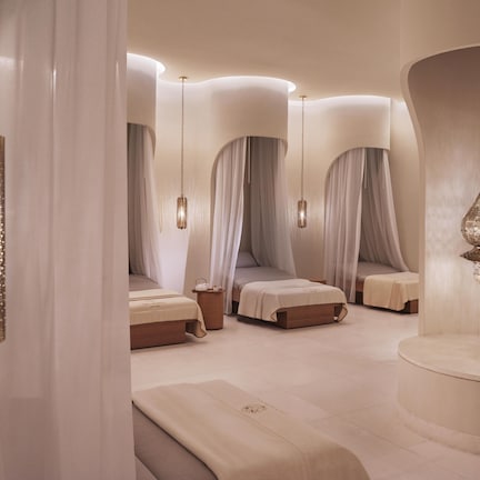 A modern spa room with a curved ceiling, multiple beds with canopy beds, and hanging lamps.