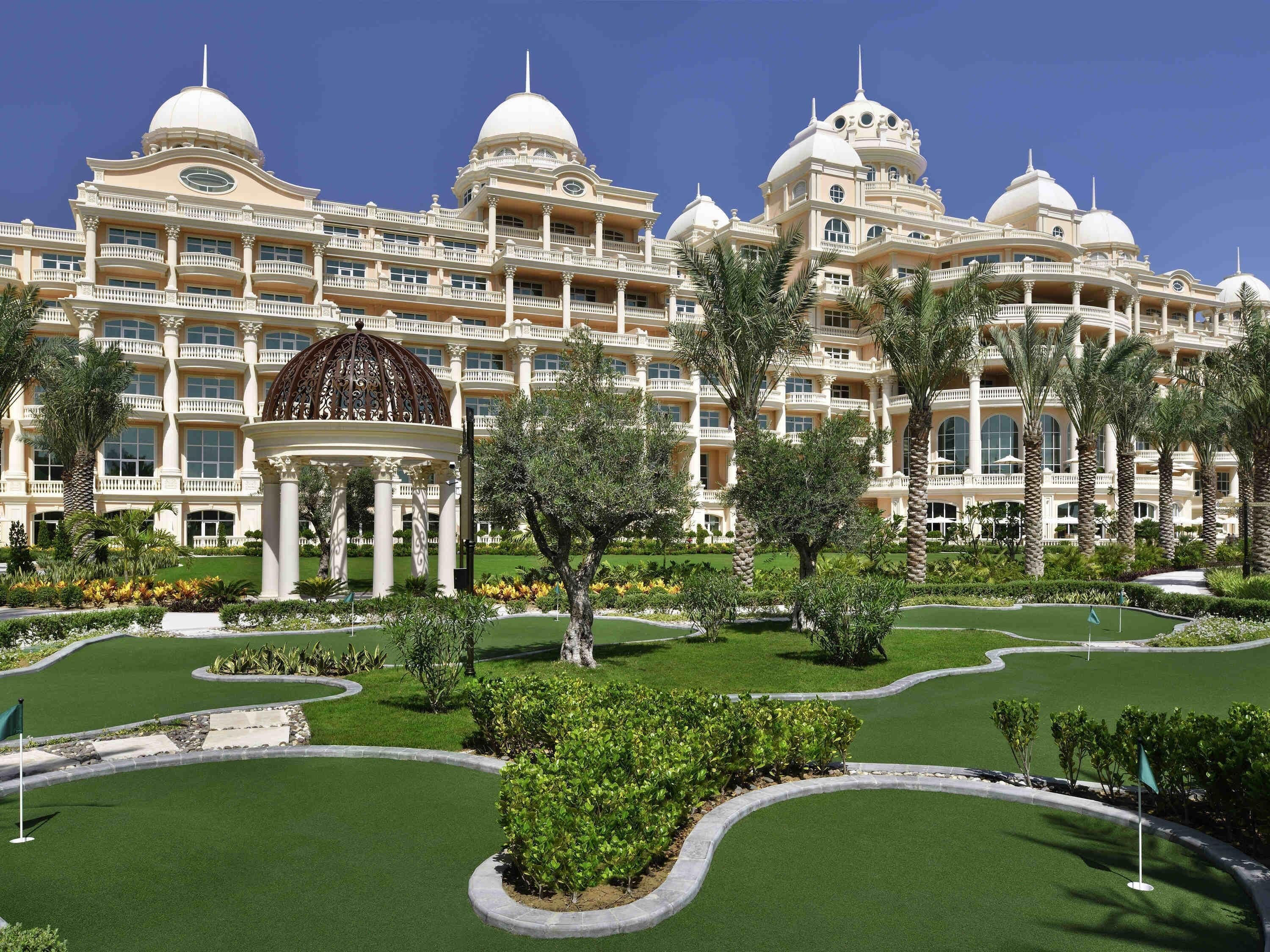 A large, multi-story hotel with a central dome structure, surrounded by manicured gardens and palm trees.