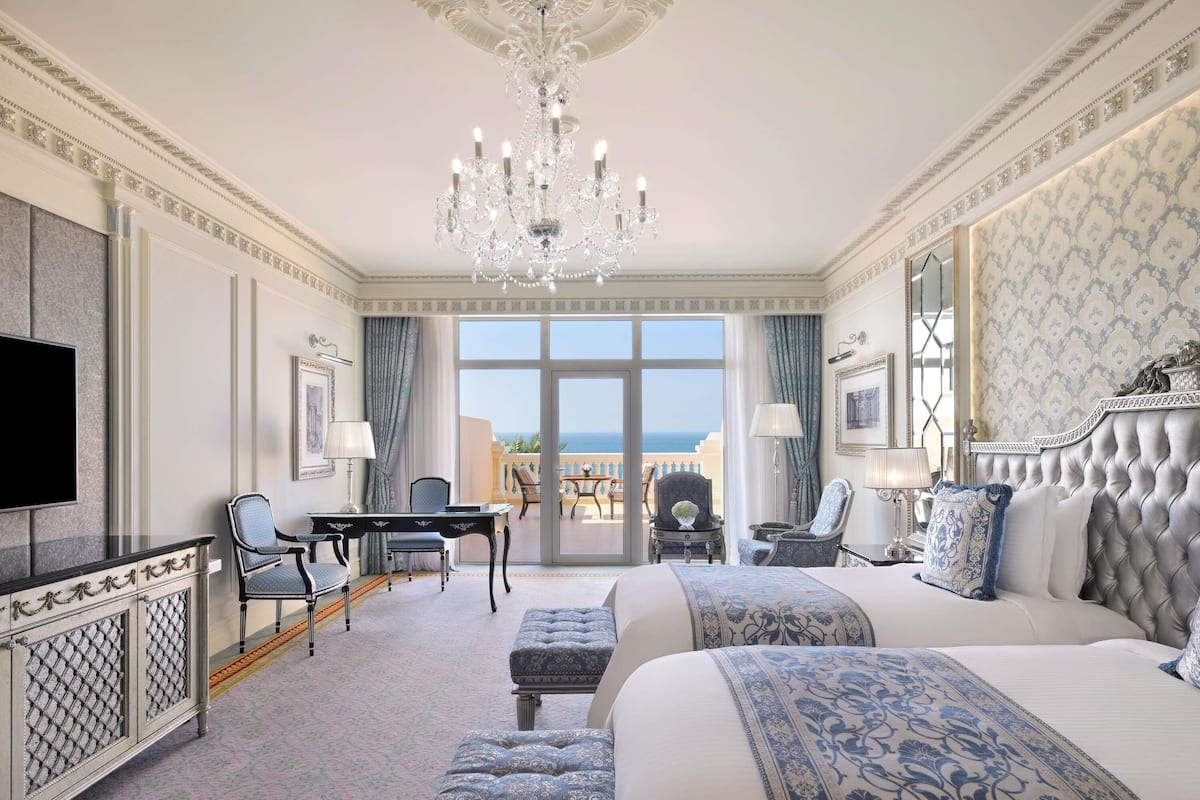 A hotel room with a large bed, a desk, two chairs, a television, and a view of the sea.
