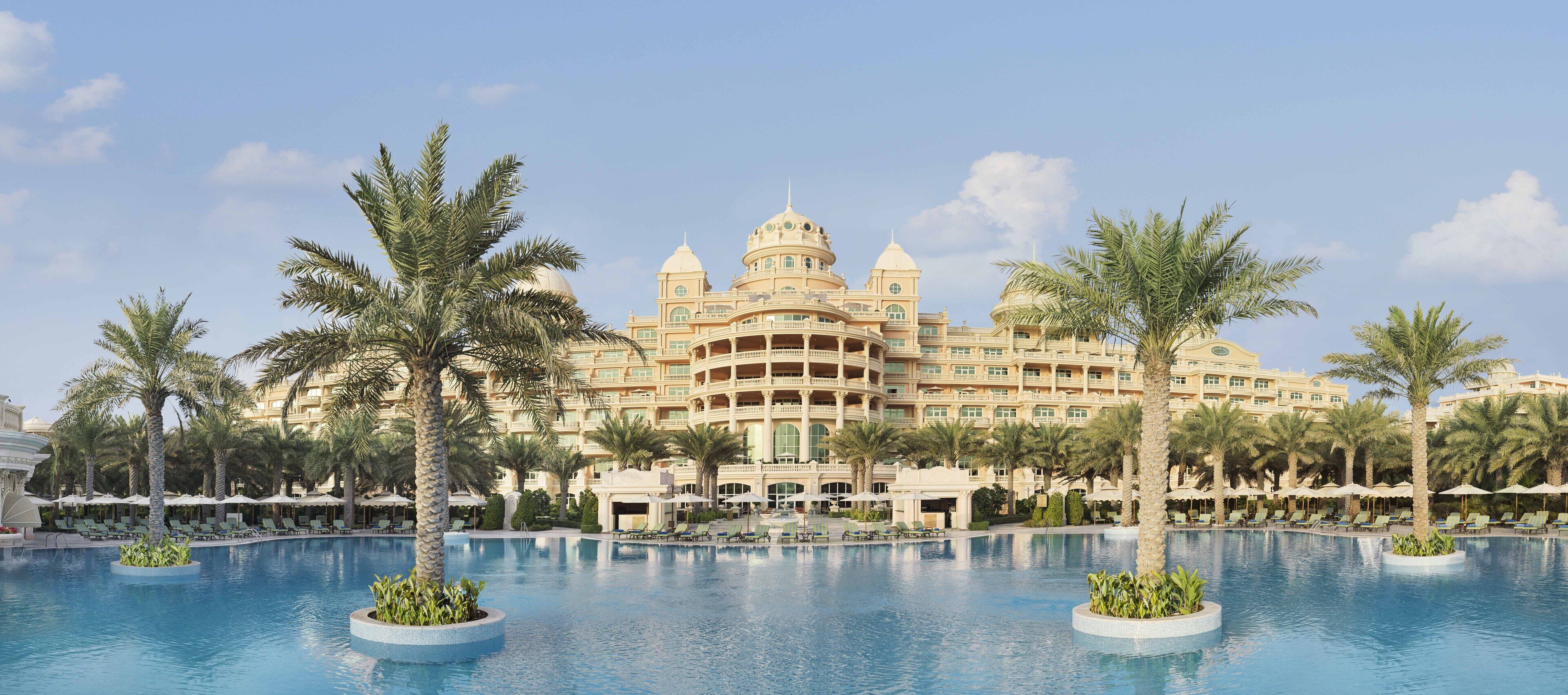 A large hotel with multiple balconies and a central courtyard with a swimming pool.