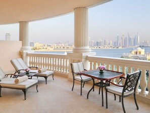 A balcony with a city view, a table with a vase, and two lounge chairs. - Raffles The Palm (Dubai)