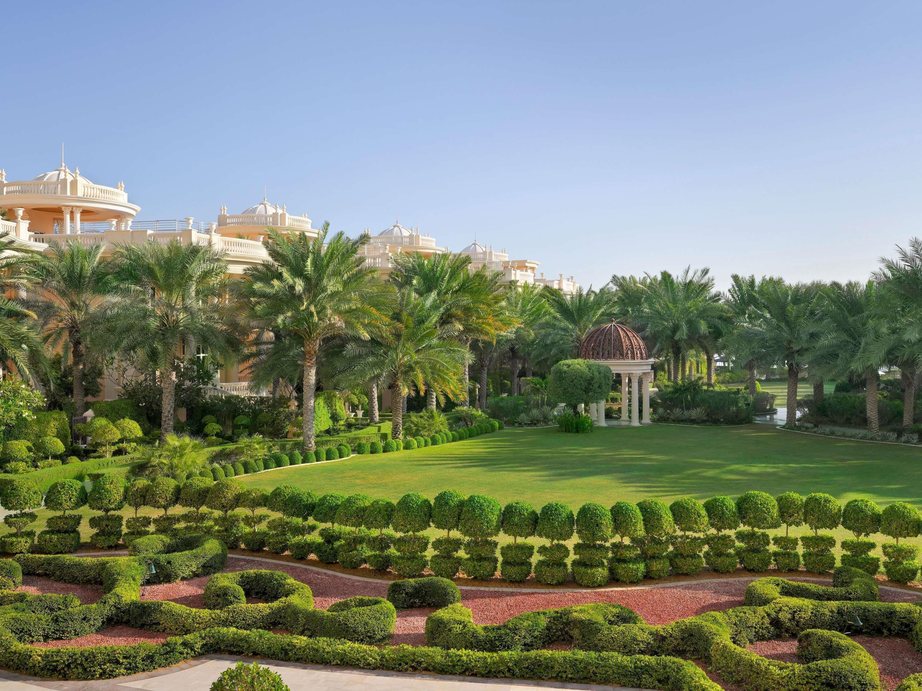 A landscaped garden with a gazebo, palm trees, and a large building with domed structures.