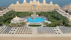 A large resort with a central pool, multiple guest rooms, and a beach area with sun loungers. - Raffles The Palm (Dubai)
