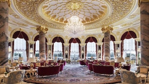 A grand lobby with ornate gold ceiling, large chandeliers, and plush red seating.