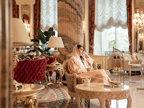 A luxurious room with ornate furniture, a red velvet armchair, a white sofa, and a decorative table with a teapot and a birdcage.