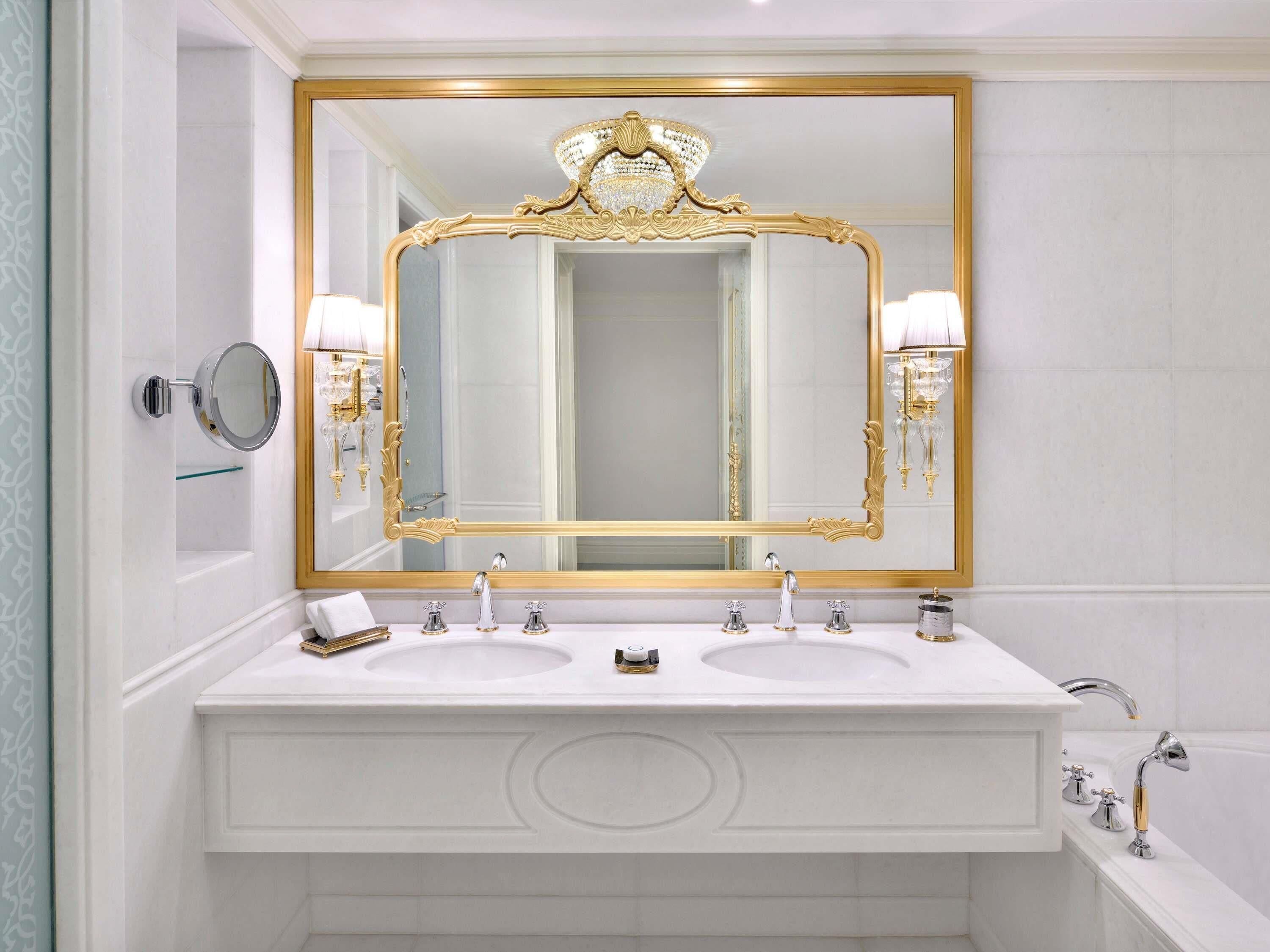 A bathroom with two sinks, a large mirror with a gold frame, and a bathtub.