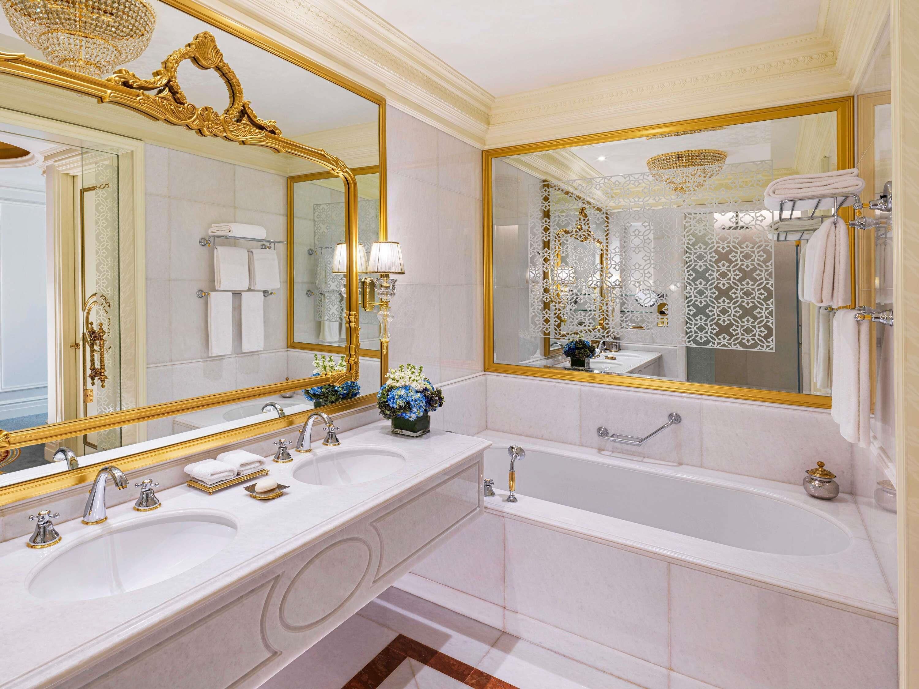 A luxurious bathroom with a large mirror, two sinks, a bathtub, and decorative flowers.