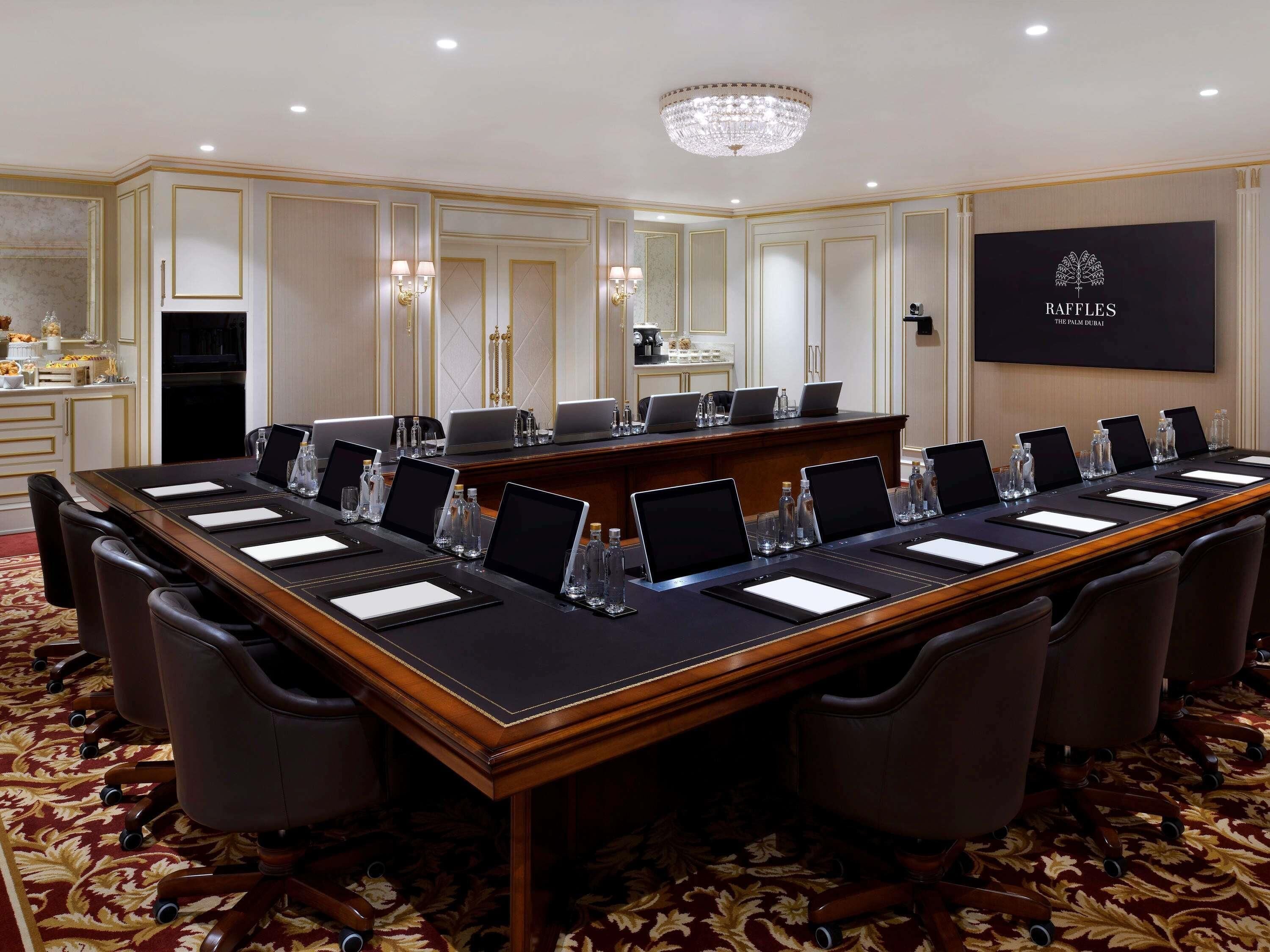 A conference room with a long table, chairs, laptops, water bottles, and a chandelier.