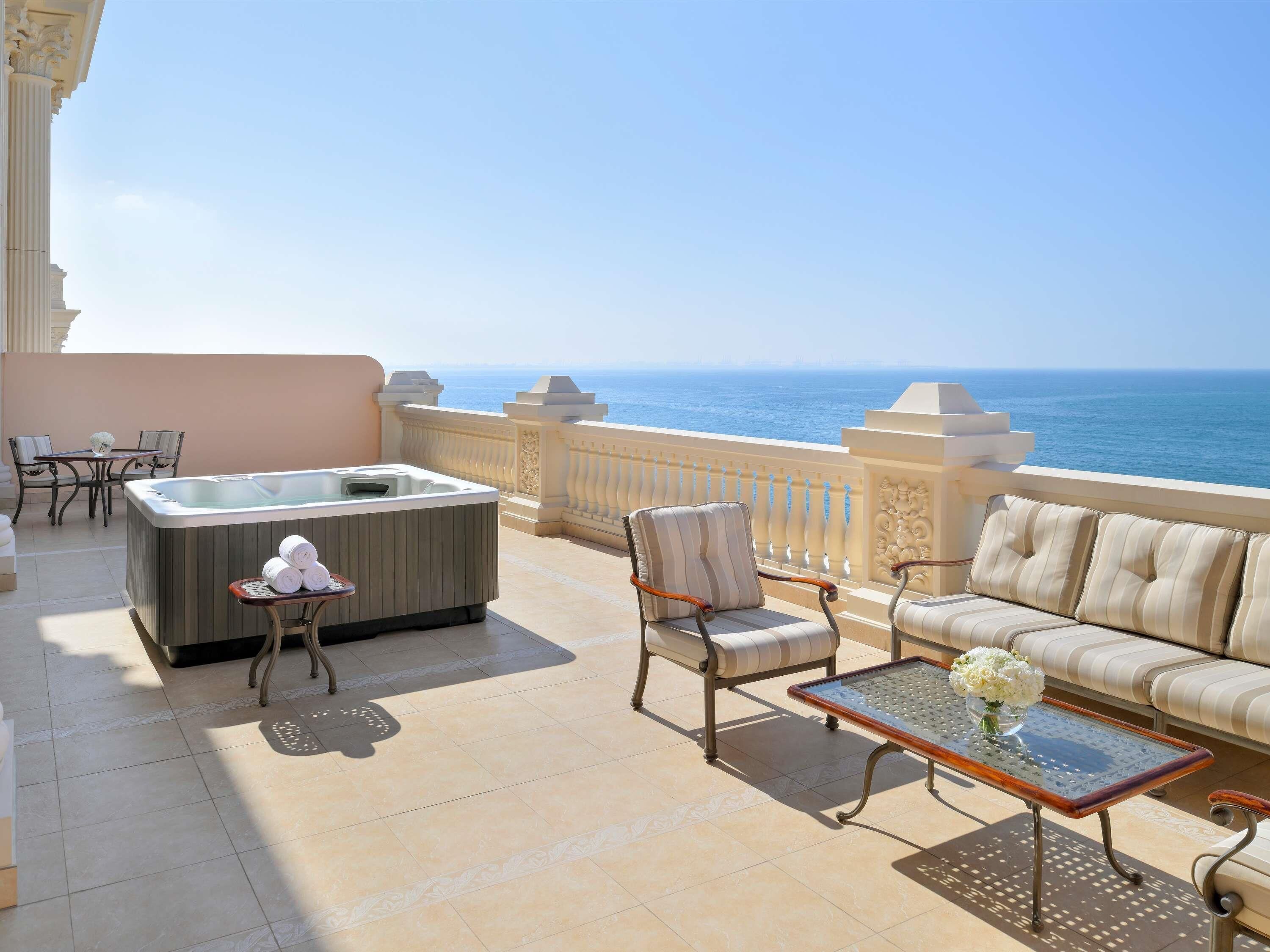 A balcony with a hot tub, seating, and a view of the sea.