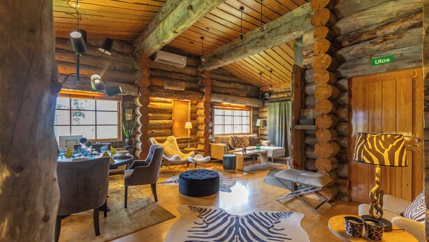 A log cabin interior with a dining area, seating, and a fireplace. - Kuukkeli Log Houses Teerenpesä - Premium Suite A48 (Saariselka)