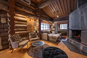 A log cabin interior with a fireplace, wooden walls, and a cozy seating area. - Kuukkeli Log Houses Teerenpesä - Premium Suite A48 (Saariselka)