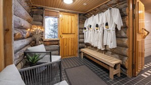 A log cabin interior with a wooden bench, a seating area with cushions, and a wall-mounted robe rack. - Kuukkeli Log Houses Teerenpesä - Premium Suite A48 (Saariselka)