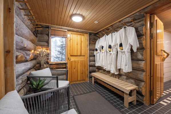 A log cabin interior with a wooden bench, a seating area with cushions, and a wall-mounted robe rack. - Kuukkeli Log Houses Teerenpesä - Premium Suite A48 (Saariselka)