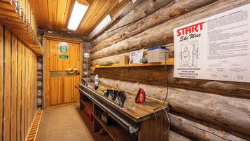 Interior de uma cabana de madeira com uma porta de madeira com a inscrição 'Ulos', um banco de madeira, uma prateleira com objetos e um cartaz com o título 'START Ski Wax'.