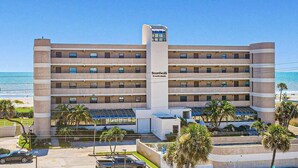 Un hotel de varios pisos con una torre central, balcones y vistas a la playa.