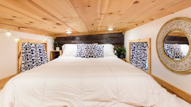 A large bed with a white bedspread and blue patterned pillows in a room with wooden flooring and a wooden ceiling. - True Tiny Home & Community l 4 Mi To Mentone (Mentone)