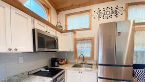 A compact kitchen with white cabinets, a stainless steel refrigerator, a microwave, and a sink. - True Tiny Home & Community l 4 Mi To Mentone (Mentone)