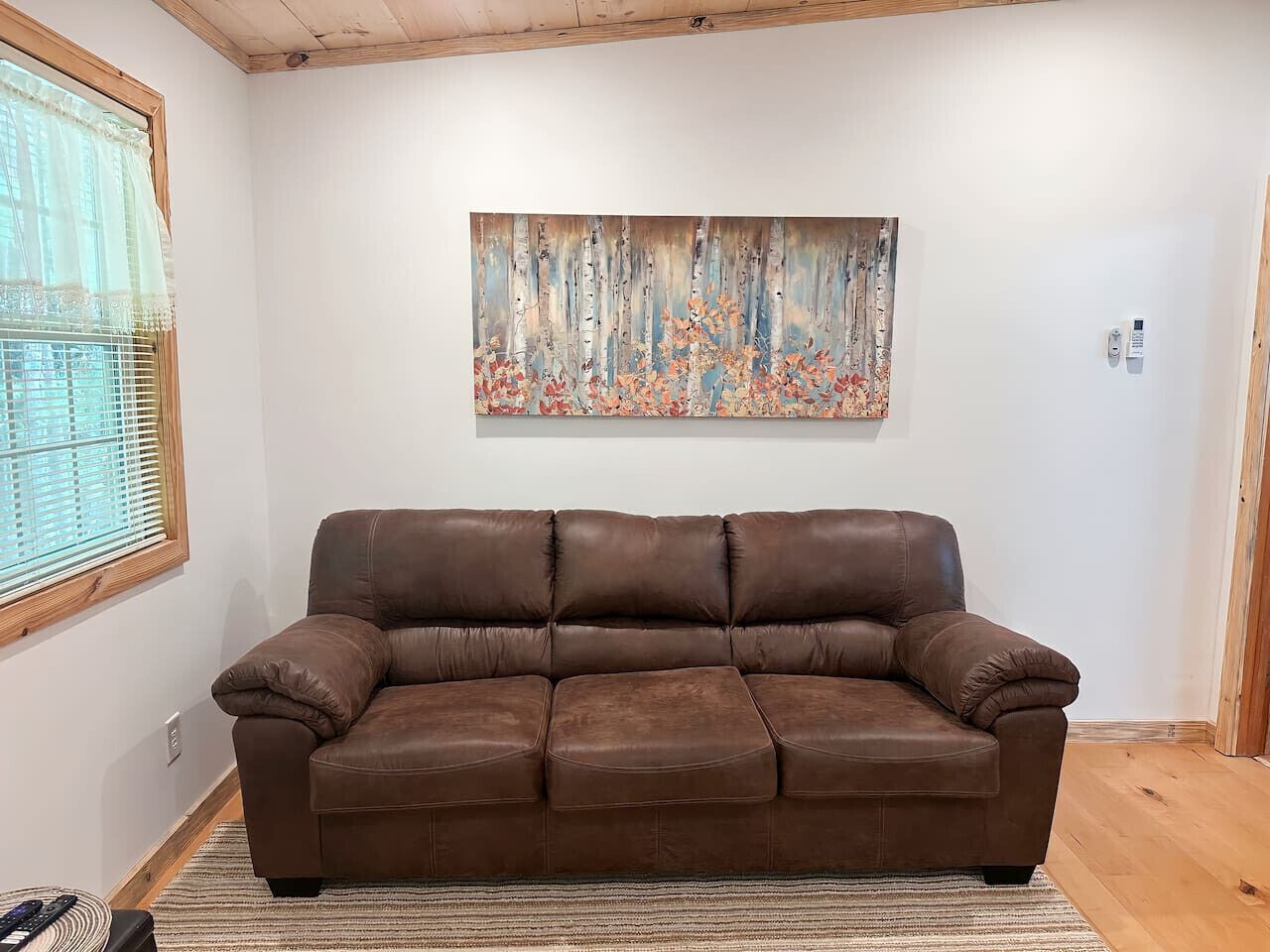 A brown leather sofa in a room with a wooden ceiling and a painting on the wall.