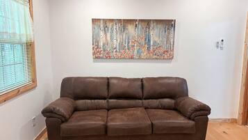 A brown leather sofa in a room with a wooden ceiling and a painting on the wall.