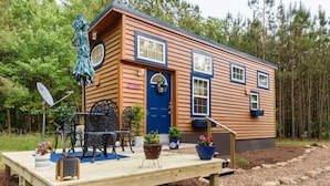 A wooden cabin with a blue door, windows, and a deck with outdoor furniture and potted plants. - True Tiny Home & Community l 4 Mi To Mentone (Mentone)