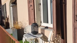 A balcony with a table and chairs, a potted plant, and a window with shutters.
