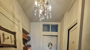 A hallway with a wooden herringbone floor, a chandelier, a door with a wreath, and a framed picture on the wall.
