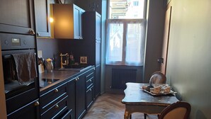 A kitchen with dark cabinetry, a wooden herringbone floor, a dining table with chairs, and a chandelier.