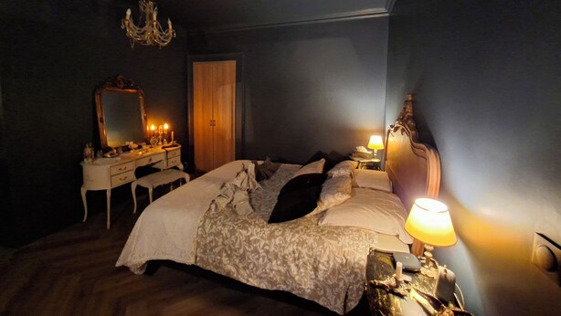 A bedroom with a bed, bedside table, lamp, dresser, mirror, and a chandelier.