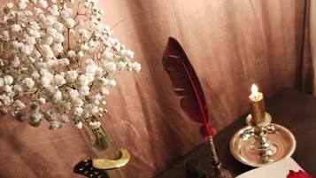 Une table ornée d’un vase de fleurs blanches, d’une plume d’oie, d’une bougie, d’un livre et d’une rose rouge.