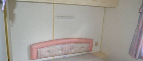 A small, single-bed room with a headboard, a bedside table, and a wardrobe above the bed.