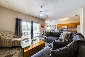A living room with a sofa, armchairs, a glass coffee table, and a ceiling fan.