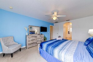 A bedroom with a bed, a chair, a dresser, a ceiling fan, and a TV.