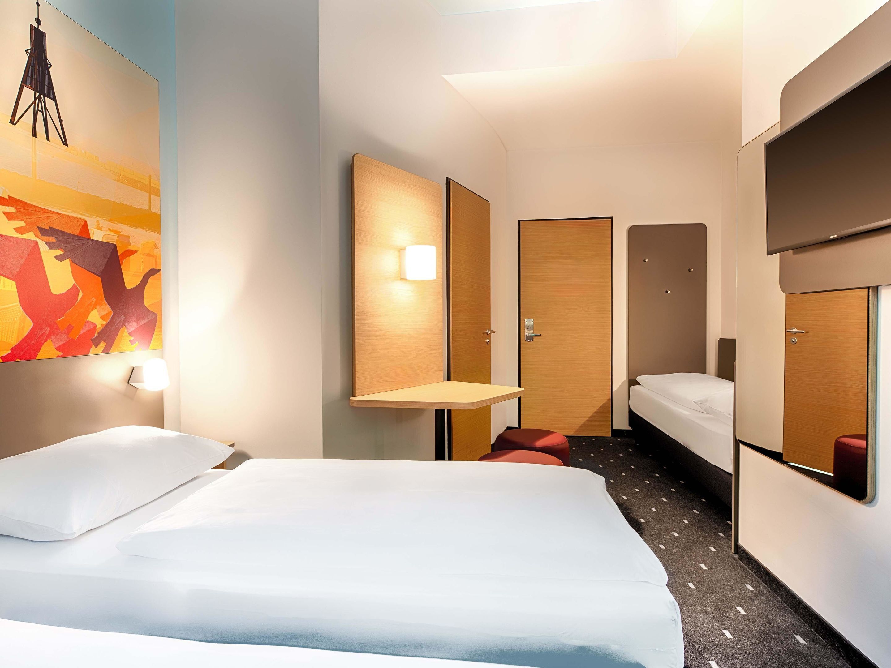 Habitación de hotel con una cama grande, una mesita pequeña, un televisor montado en la pared y un cuadro.