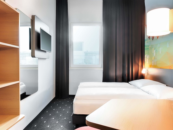Habitación de hotel con cama, televisor montado en la pared, ventana con cortinas y un cuadro en la pared.