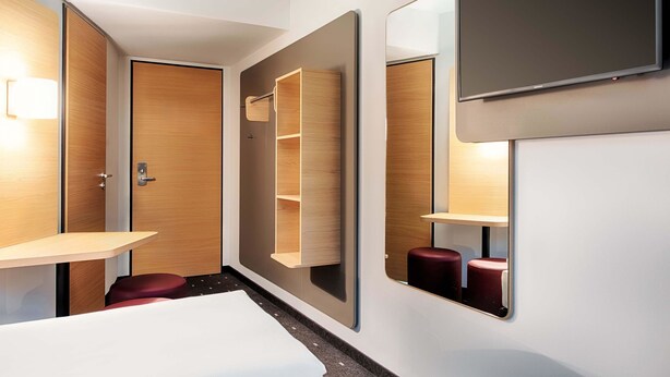 Una habitación de hotel moderna con una cama, un televisor montado en la pared, un armario de madera y una pequeña mesa.