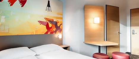 A hotel room with a bed, a red ottoman, a wall-mounted light, and a large abstract painting.